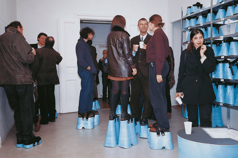 a photograph of people standing on blue plastic stilts of differing lengths such that they're all the same height