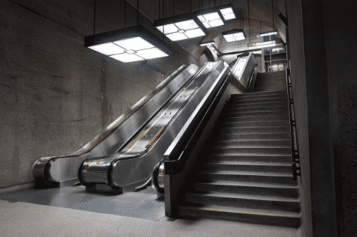 A photograph of the montreal bonaventure metro interior, showing two escalators and a set of stairs. it's brightly lit, all concrete and metal.